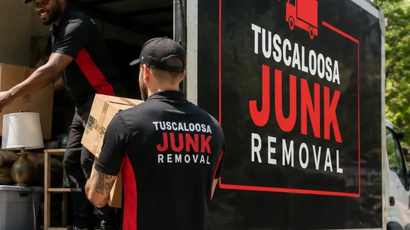Junk removal crew member carrying a moving box beside a truck in Tuscaloosa